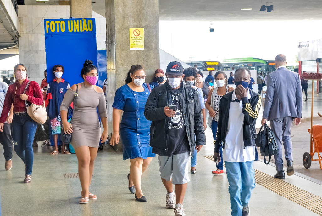 Pessoas de máscara, de várias idades, raças e gêneros, caminhando na calçada